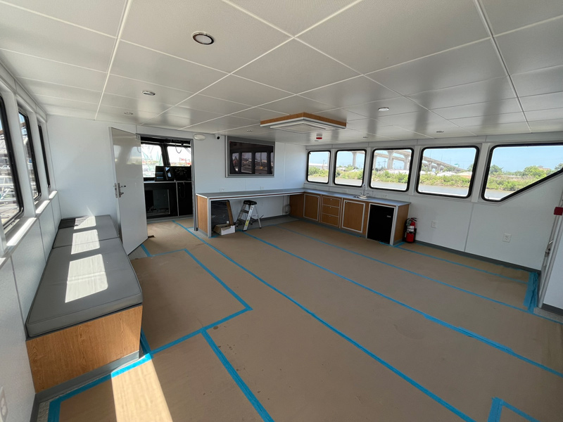 Learn about the spacious cabin interior featuring large windows, built-in bench seating, a counter with stools, and a small kitchenette. Blue tape lines mark floor areas, with a fire extinguisher visible near the corner.