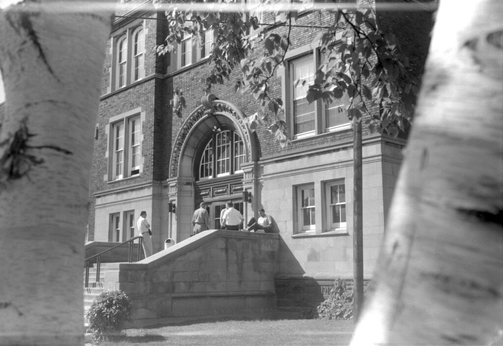 Black and white photo of students hanging out outside of campus building