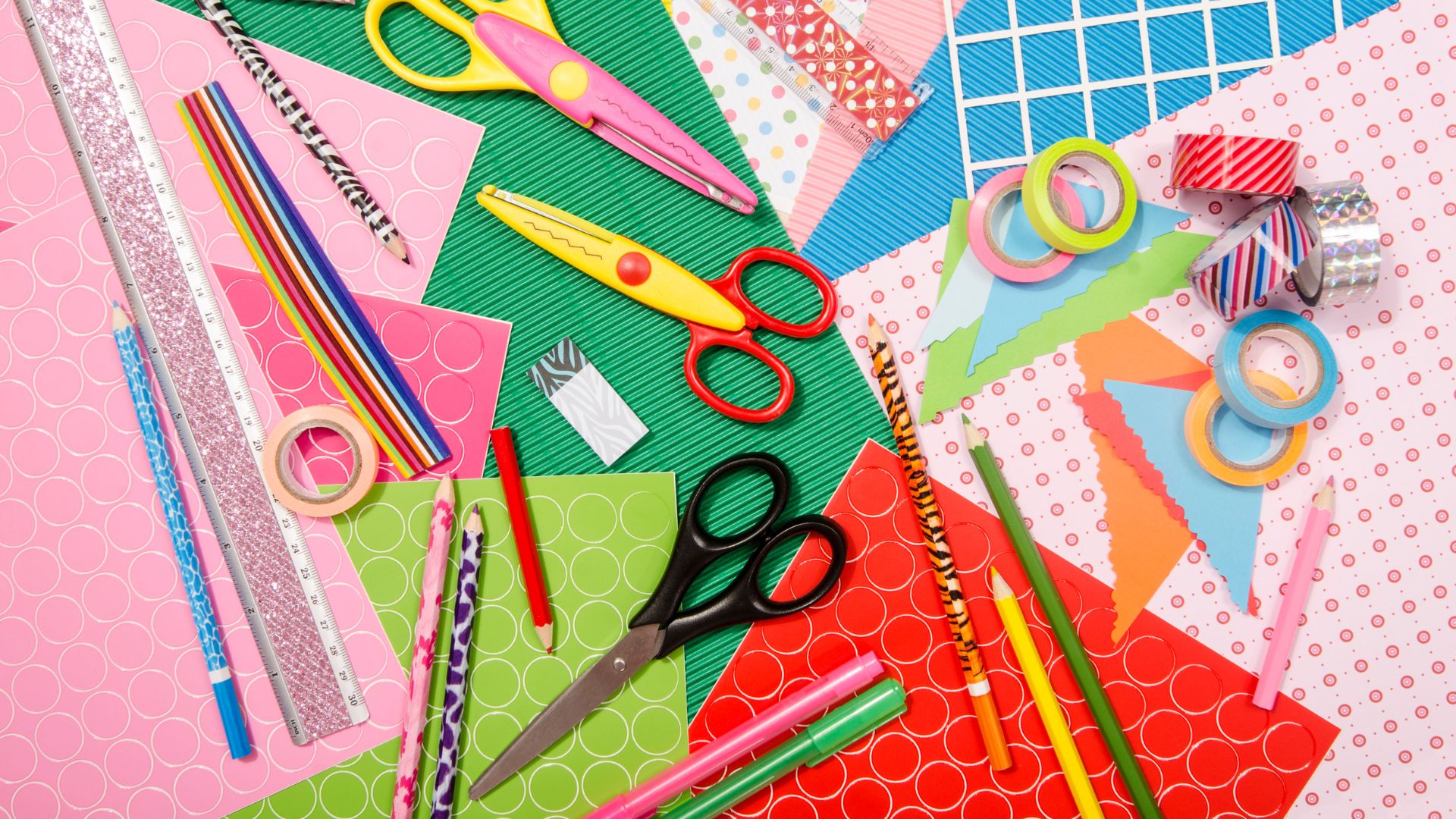 Colorful craft supplies on a table, including patterned paper, scissors, pencils, pens, washi tape, and striped straws, all arranged in a scattered, creative layout.
