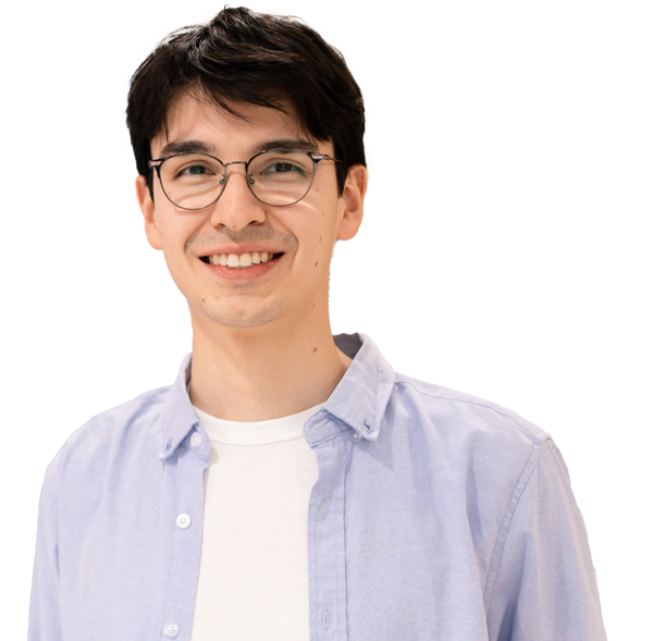 Lucas Palomino with short brown hair and glasses smiles at the camera. He is wearing a light blue button-up shirt over a white t-shirt, with a soft, blurred background in blue and beige tones at the University of Wisconsin-Superior.