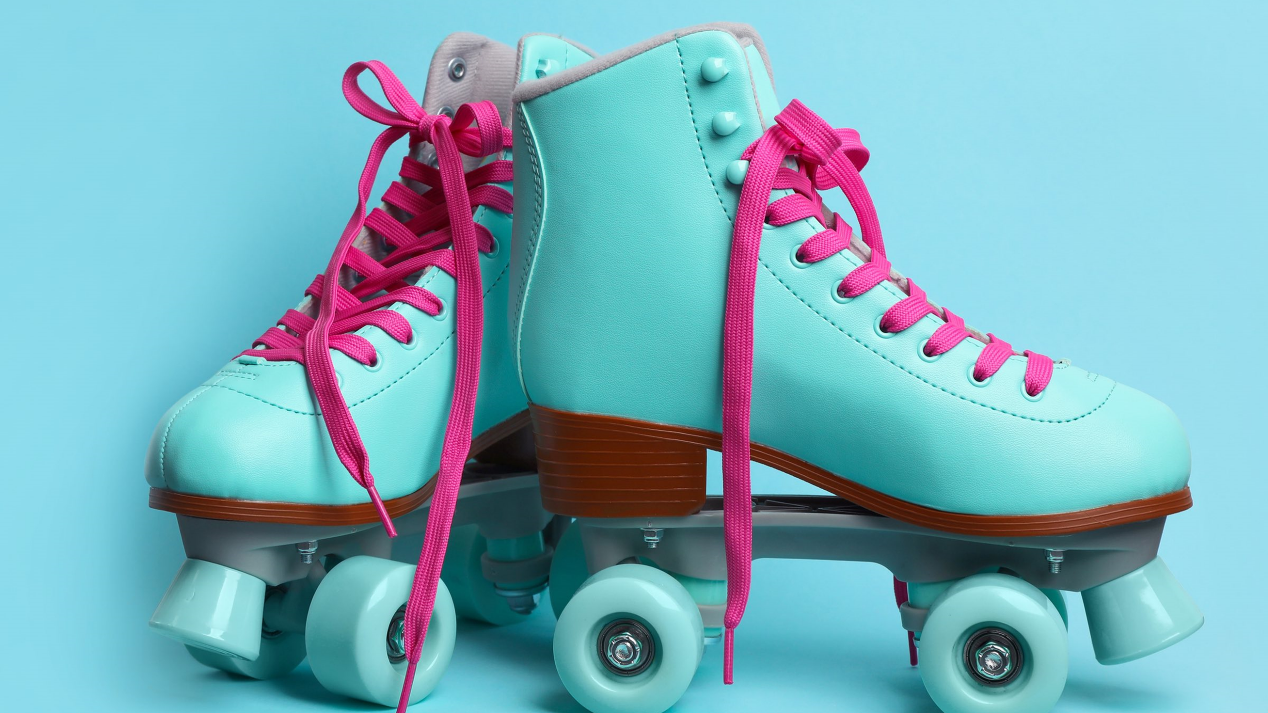 A pair of vintage-style teal roller skates with bright pink laces and brown soles, set against a solid light blue background.