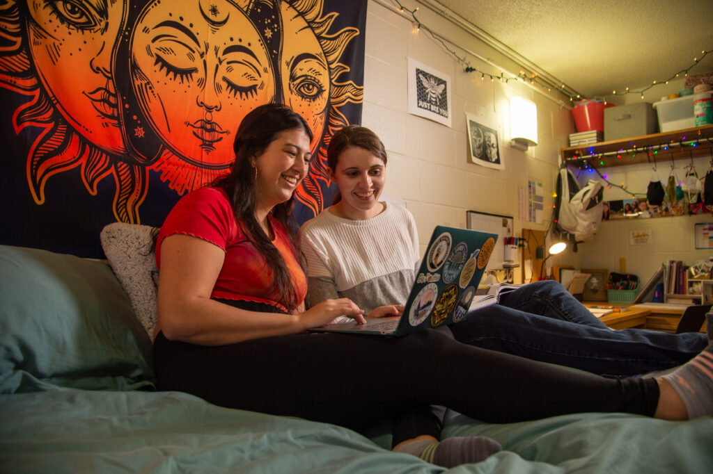 Students sitting in a residence hall looking at a computer