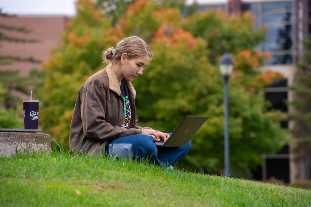 Student sitting on grass and using laptop