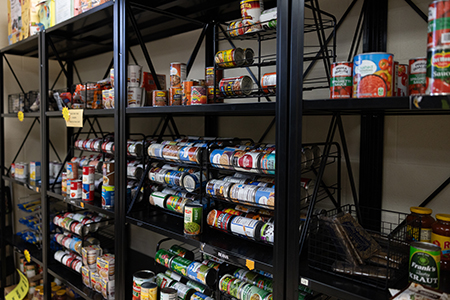 Shelves filled with various canned goods, including vegetables, soups, and beans, organized in rows at a food pantry or storage area.