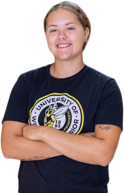 A student with short hair smiles with arms crossed, wearing a black T-shirt featuring a yellow bee and the words University of Wisconsin-Superior. Tattoos are visible on both forearms.