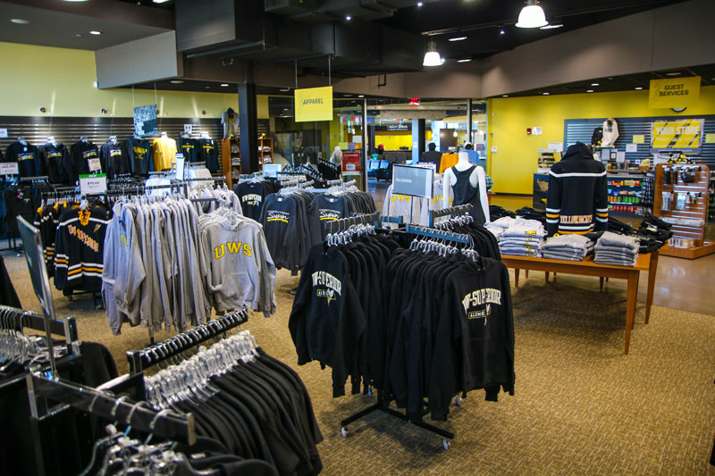 A campus bookstore interior at Yellowjacket Union showcases racks of university-branded clothing, including hoodies and sweatshirts in black, gray, and yellow, with a guest services counter and shelves in the background.