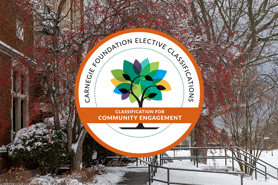 A round badge reading Carnegie Foundation Elective Classifications: Classification for Community Engagement is overlaid on a snowy campus scene with red-berried trees and a brick building in the background.the University of Wisconsin-Superior has been selected for the Carnegie Elective Classification for Community Engagement