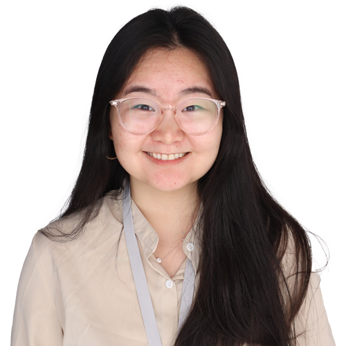 A young woman with long black hair and clear glasses smiles at the camera, embodying confidence and superior outcomes. She is wearing a beige blouse and a gray lanyard with a badge against a plain white background.